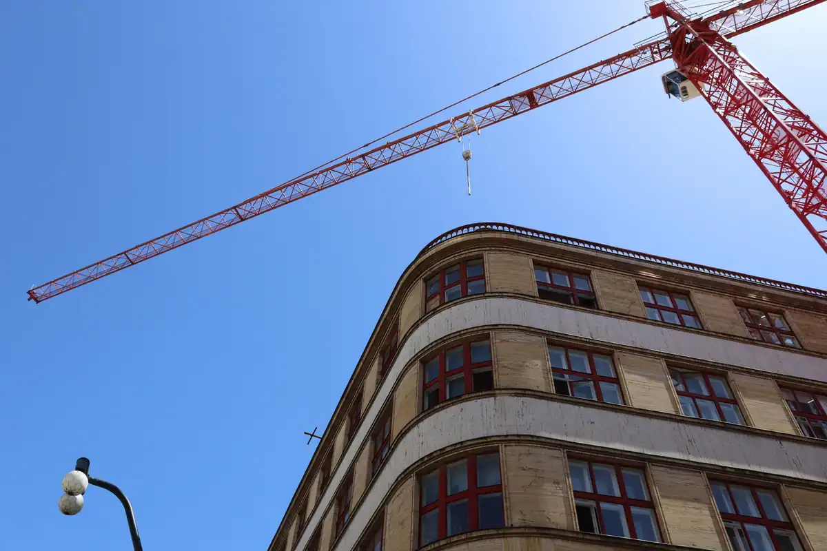 Macara de construcții lângă fațada unui bloc nou, pe cer albastru