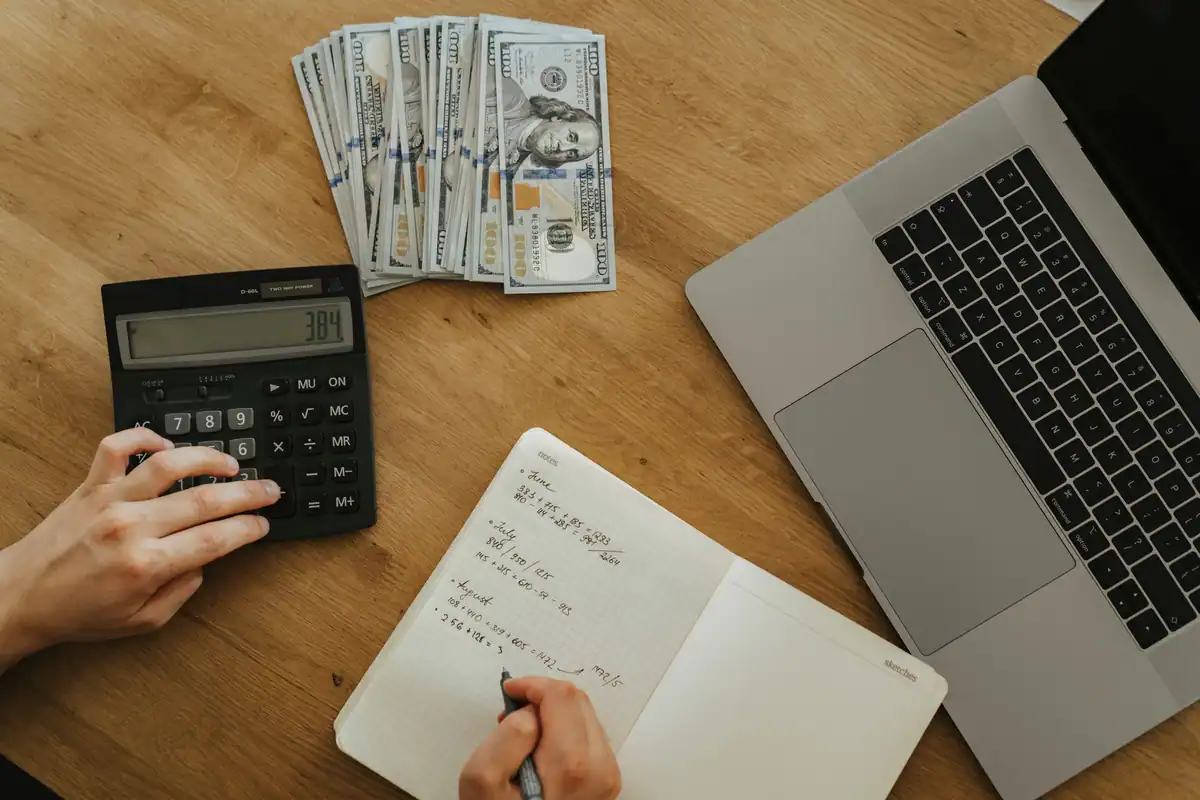 Mâini care folosesc un calculator și un caiet pentru a planifica avansul