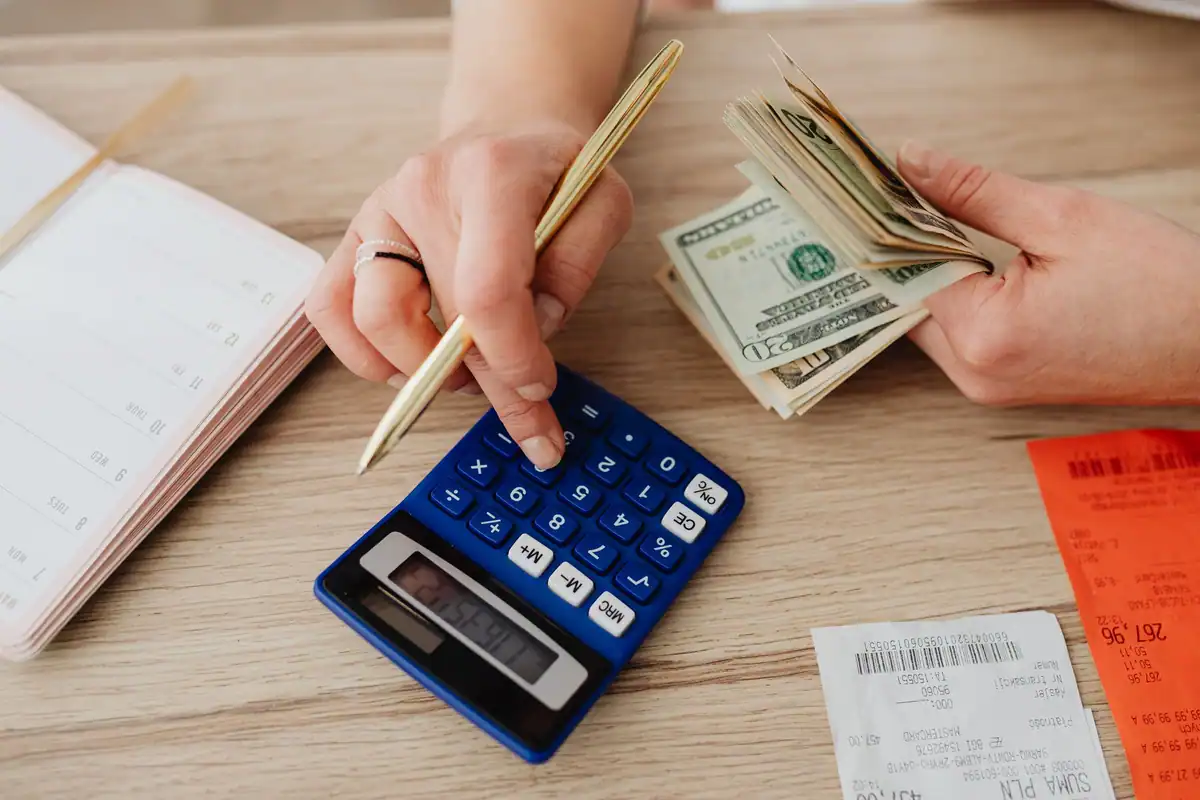 Mâini care numără bani lângă un calculator pentru a stabili bugetul chiriei