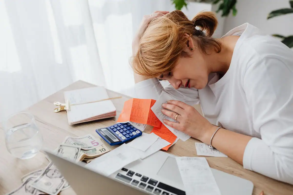 Femeie copleșită de facturi, cu calculator și bani pe masa din sufragerie