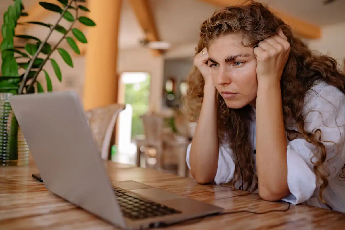 Femeie concentrată care verifică atent un anunț pe laptop, acasă