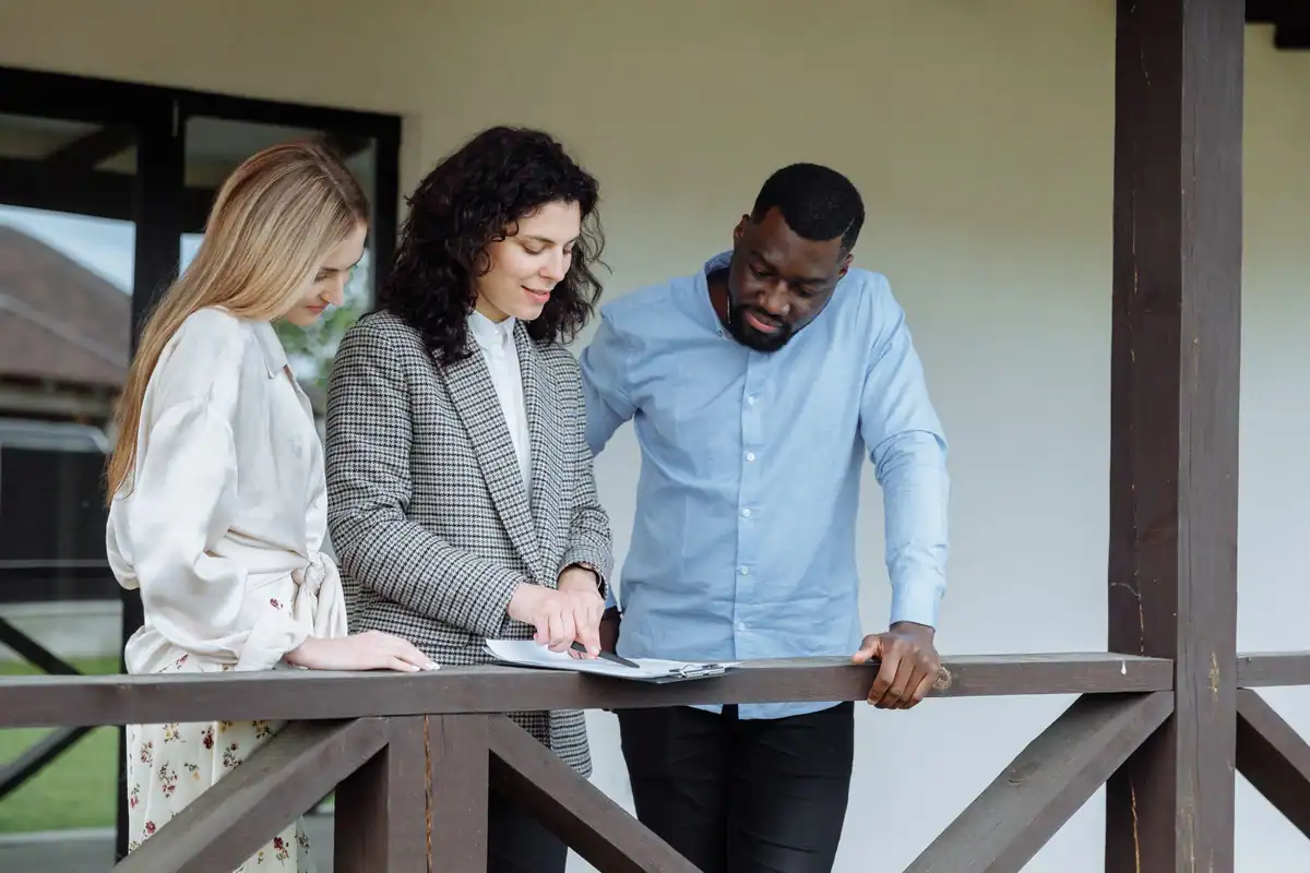 Agent imobiliar care discută actele proprietății cu un cuplu pe verandă