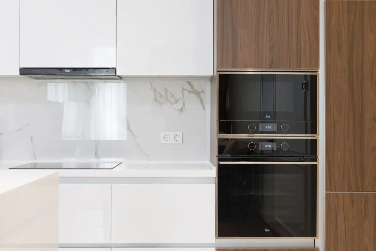 Bucătărie albă cu lemn, dulapuri și electrocasnice încorporate într-un apartament modern